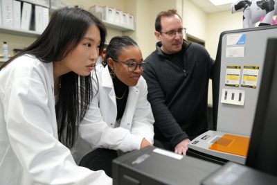 Tim Jarome and two students in lab coats study a computer screen.