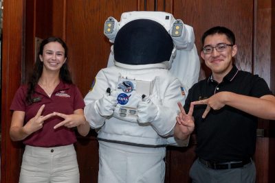 Maggie Campbell and Kevin Xu proudly showcase their VT hand gesture in front of astronaut suit in Houston.
